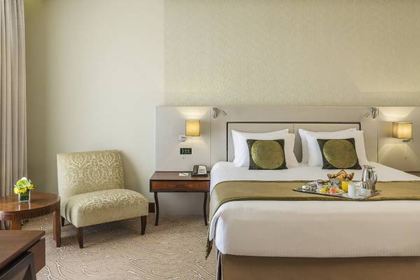 Ein elegantes Hotelzimmer im Tower Plaza Hotel Dubai mit einem großen Bett, einem Frühstückstablett und einem gemusterten Stuhl.