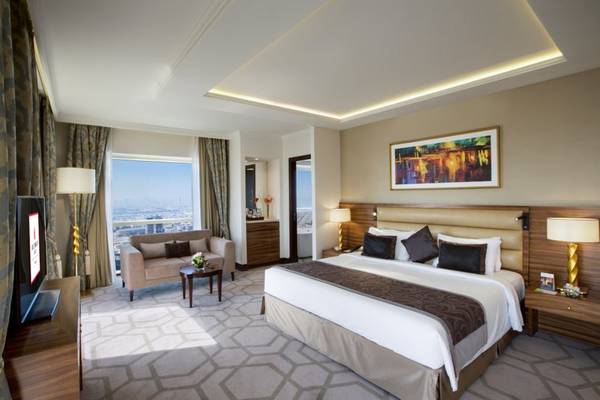 Suite-Zimmer im Tower Plaza Hotel Dubai mit großem Bett, Wohnzimmerbereich und Panoramafenster.