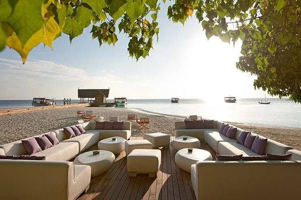 Loungebereich am Strand des Constance Moofushi Maldives Hotels mit weißen Sofas und Tischen.