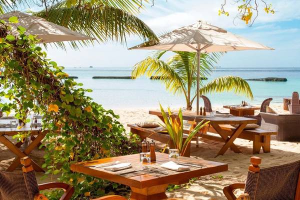 Außenbereich des Constance Moofushi Maldives mit Tischen und Stühlen am Strand und Palmen