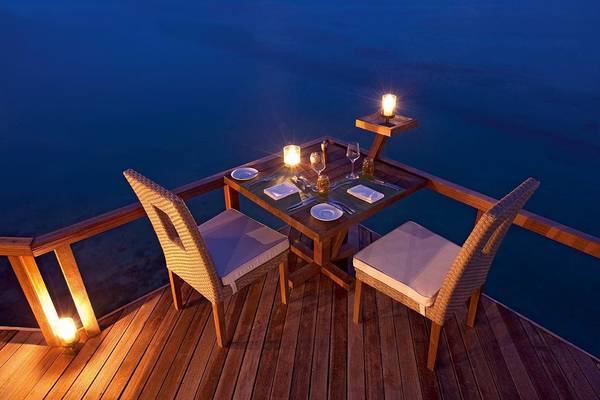 Ein Tisch auf einer Terrasse am Meer im Constance Moofushi Maldives mit zwei Kerzen und einem Glas Wein.