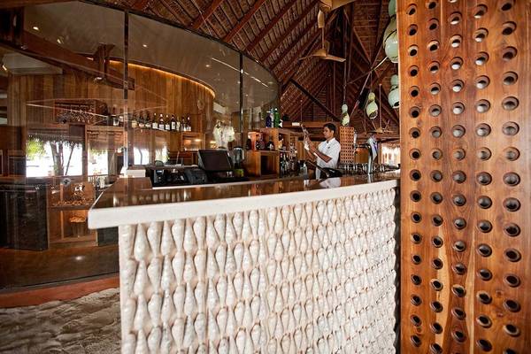 Innenansicht der Bar im Constance Moofushi Maldives Hotel mit Barkeeper, Holzelementen und Bartisch.