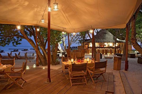 Abendessen auf dem Strand im Constance Moofushi Maldives mit Tisch und Stühlen unter einem Dach.
