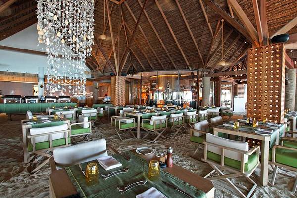 Innenraum des Constance Moofushi Maldives Restaurants mit Holzstühlen und Tischen auf Sandboden.