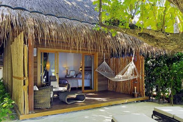 Außenbereich eines Bungalows des Constance Moofushi Maldives mit Hängematte, Möbeln und Blick auf das Innere.