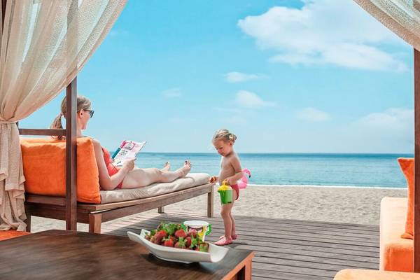 Eine Frau liest auf einer Terrasse im Aska Lara Resort & Spa, während ein Kind daneben spielt.