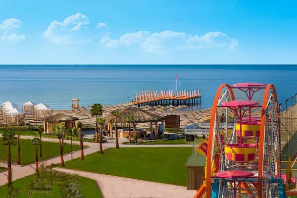 Außenansicht des Aska Lara Resort & Spa mit Blick auf den Strand, Pier und Fahrgeschäft.