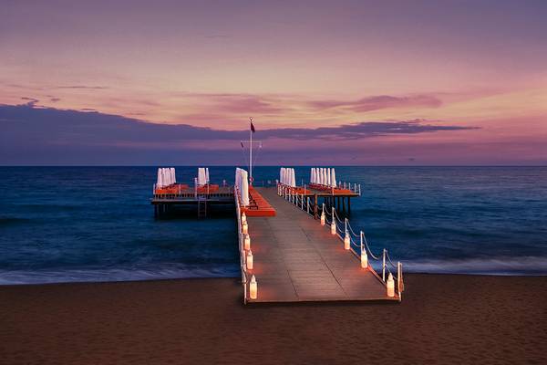 Aska Lara Resort & Spa Pier am Meer bei Sonnenuntergang mit roten Liegen und Laternen