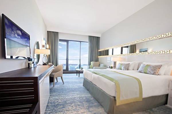 Innenansicht eines Zimmers im JA Ocean View Hotel mit großem Bett, Fernseher und Meerblick.