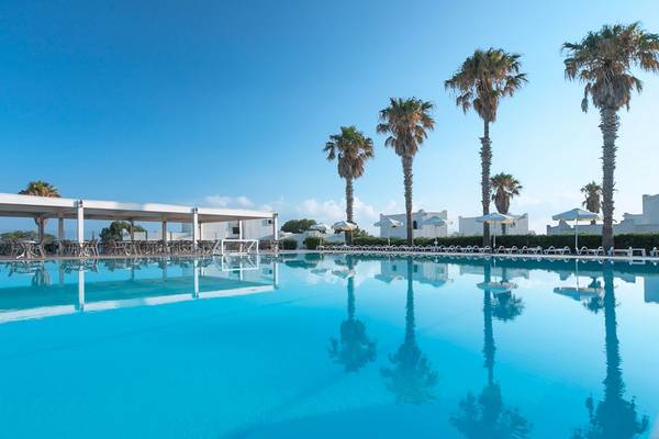 Außenpool des Aeolos Beach Hotel in Kos mit Sonnenliegen und Palmen im Hintergrund.