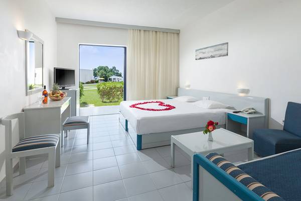 Zimmer im Aeolos Beach Hotel mit Herz-Dekoration auf dem Bett und Blick auf den Garten.