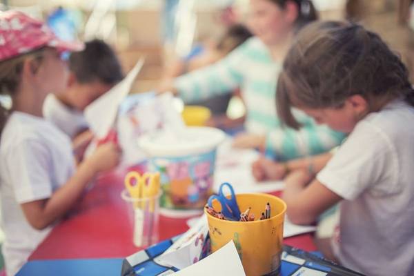 Kinder sitzen an einem Tisch und basteln mit Papier, Scheren und Stiften.