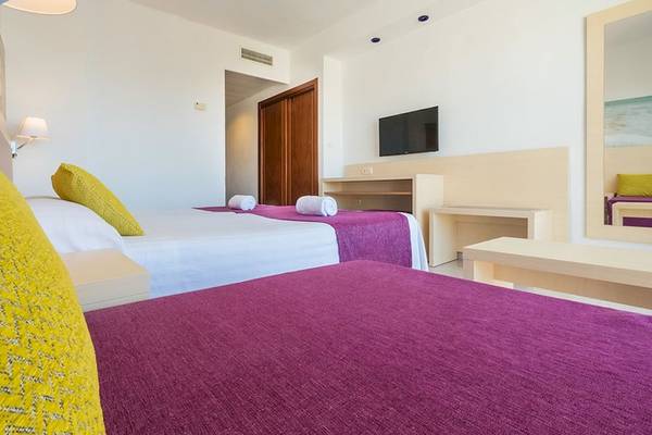 Doppelzimmer im Moon Dreams Coral Beach Hotel mit zwei Betten, bunten Decken und Kissen, Fernseher an der Wand und einem Schreibtisch.