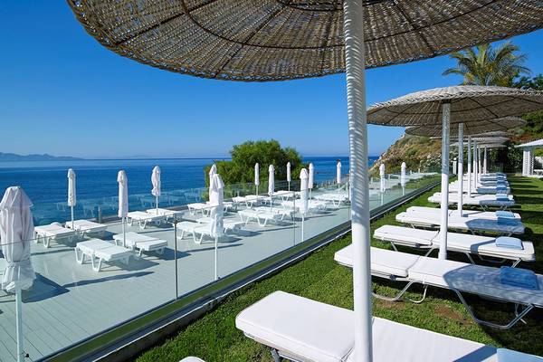 Außenbereich des Dimitra Beach Hotel mit weißen Liegen und Sonnenschirmen am Meer