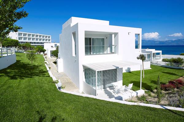 Außenansicht des Dimitra Beach Hotel & Suites mit grüner Wiese und Meer im Hintergrund.