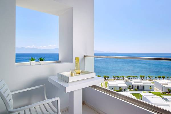 Balkon mit Meerblick im Dimitra Beach Hotel mit weißen Möbeln und Pflanzen im Fenster.