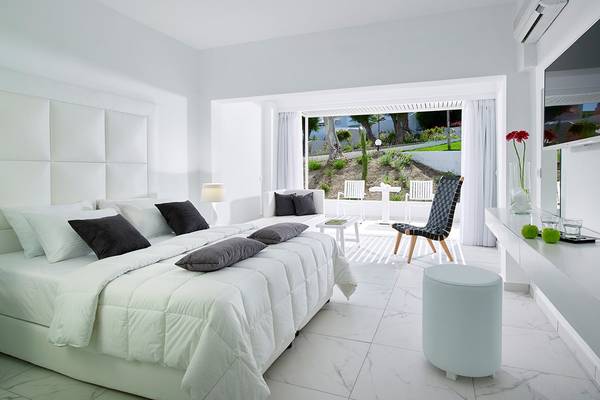 Schlafzimmer im Dimitra Beach Hotel & Suites mit weißem Bett und Möbeln, Balkonzugang und Gartenblick.