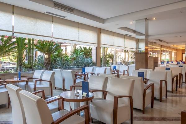Lobby-Lounge im Zafiro Tropic Hotel mit weißen Stühlen und Tischen, großen Fenstern und Pflanzen.