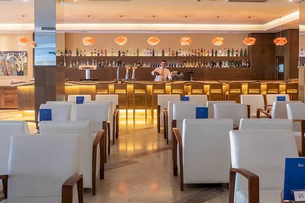 Barbereich im Zafiro Tropic Hotel mit einem Barkeeper und weißen Stühlen.