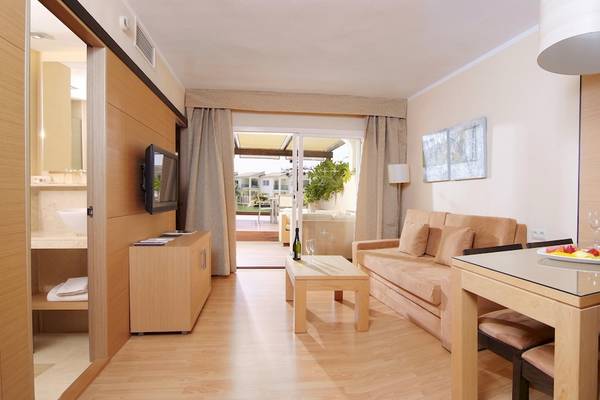 Wohnbereich des Zafiro Tropic Hotels mit Couch, Tisch, Fernseher und Glasfenstern.