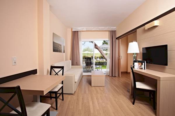 Innenansicht eines Zimmers im Zafiro Tropic Hotel mit Couch, Tisch, Fernseher und Schreibtisch.