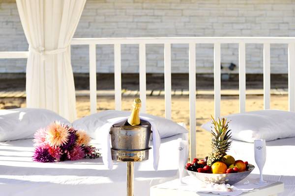 Weißes Bett mit Champagner, Obst und Blumen auf einer Terrasse.