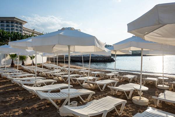 Weißes Stadt Resort Strand mit Sonnenliegen und Umbrellas, Blick auf das Meer und ein Hotelgebäude.