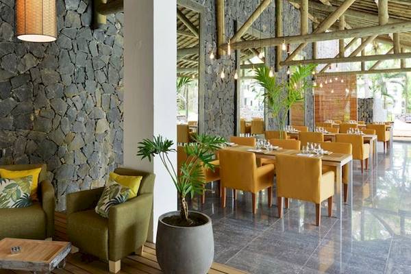 Innenansicht des Restaurants im The Ravenala Attitude Hotel mit Steinwand, grünen Stühlen und einem großen Topf