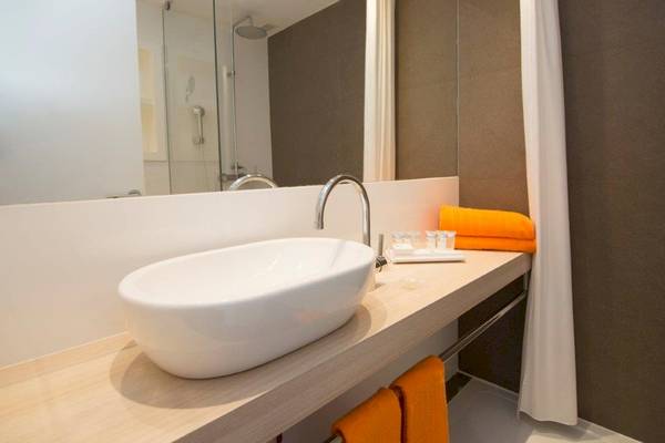 Badezimmer mit weißem Waschbecken, Spiegel und orange Handtüchern bei Ibiza Sun Apartments