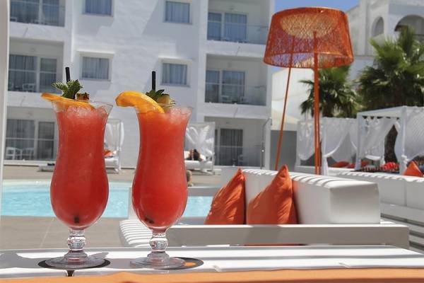 Zwei rote Cocktails auf der Terrasse vor einem Hotel mit einem Pool und Sonnenliegen.