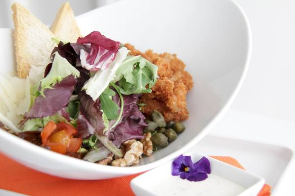 Ein weißer Teller mit gemischtem Salat, Croutons, Walnüssen und einer kleinen Beilage.