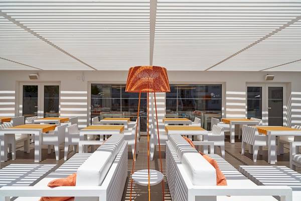 Terrasse des Ibiza Sun Apartments mit weißen Möbeln und orangefarbenen Kissen.