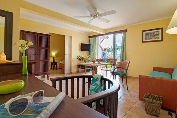 Wohnzimmer im Pierre & Vacances Village Sainte Luce mit gelben Wänden, einer Deckenventilator, einem Tisch und Stühlen.