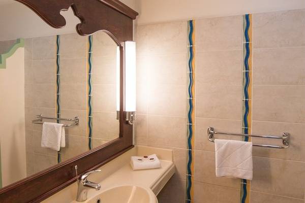 Badezimmer im Pierre & Vacances Village Sainte Luce mit Spiegel, Waschbecken, Handtüchern und Wandmustern.