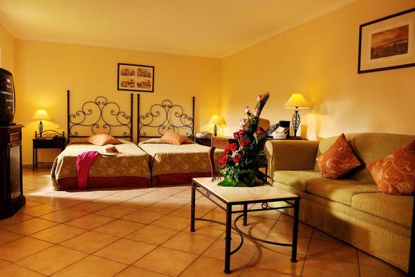 Doppelzimmer im Iberostar Playa Alameda Hotel mit zwei Betten, Sofa, Tisch, Lampen und Blumen.