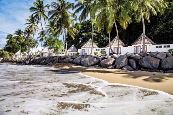 Strand mit weißen Bungalows und Palmen, geschützt durch Felsen