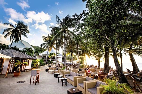 Terrasse des Langley Resort Fort Royal mit Gästen, Tischen, Stühlen und Palmen.