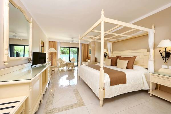 Ein Hotelzimmer im Bahia Principe Luxury Akumal mit einem Himmelbett, Fernseher und einem großen Spiegel.