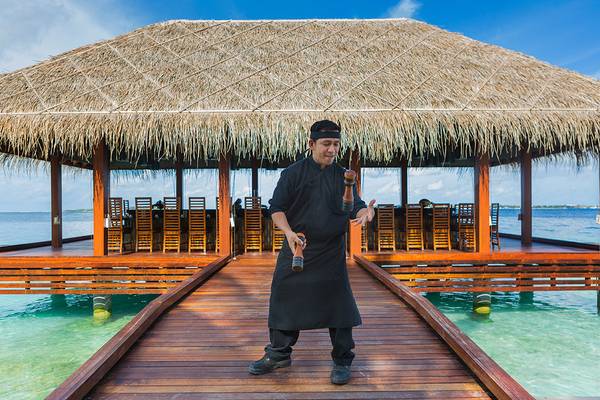 Ein Mitarbeiter des Kurumba Maldives Hotels steht auf der Terrasse und lächelt in die Kamera.