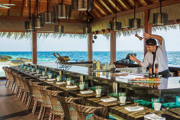 Ein Sushi-Bar im Kurumba Maldives mit Blick auf das Meer und einem Mann, der eine Zutat würzt.