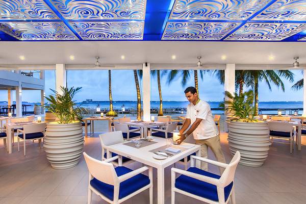 Innenansicht des Kurumba Maldives Restaurants mit Blick auf den Ozean und einem Kellner, der einen Tisch bedient.