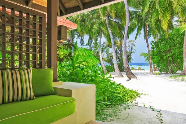 Blick auf einen weißen Strand mit Palmen und zwei Liegestühlen, vom Kurumba Maldives Hotel aus.