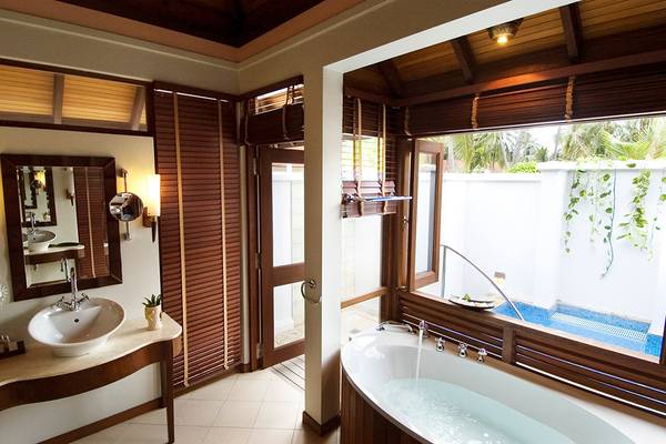 Badezimmer im Kurumba Maldives Hotel mit Badewanne und Ausblick auf den Pool.