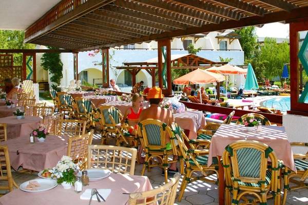 Terrasse des Gaia Village Hotels mit Gästen, Tischen und Sonnenschirmen neben einem Pool.