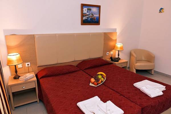 Doppelzimmer im Gaia Village Hotel mit zwei roten Betten, Früchten und Lampen.