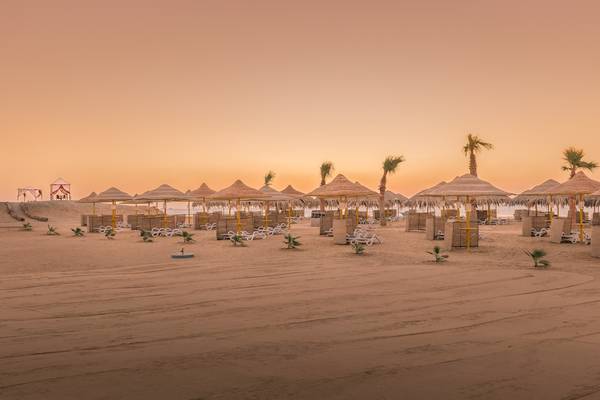Strand des Hilton Marsa Alam Nubian Resorts mit Sonnenschirmen und Liegen bei Sonnenuntergang