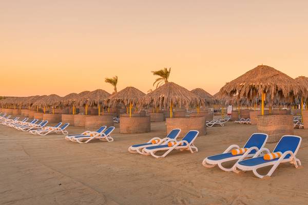 Strand des Hilton Marsa Alam Nubian Resort mit Sonnenliegen und Sonnenschirmen bei Sonnenuntergang