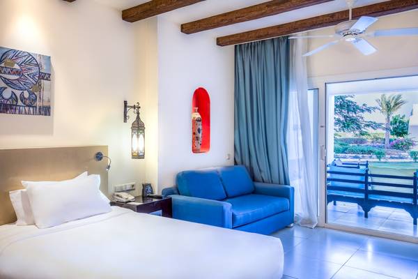 Hotelzimmer im Hilton Marsa Alam Nubian Resort mit weißem Bett, blauem Sofa und Blick auf Garten