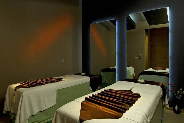 Massageraum im Blue Waters Club mit drei Massagetischen und dekorativen Blumen in der Ecke.