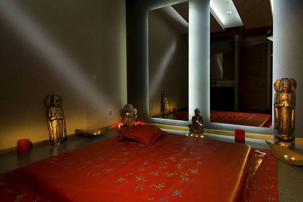 Ein Schlafzimmer mit einer roten Bettdecke, Buddha-Statuen und Spiegeln, in warmem Licht.